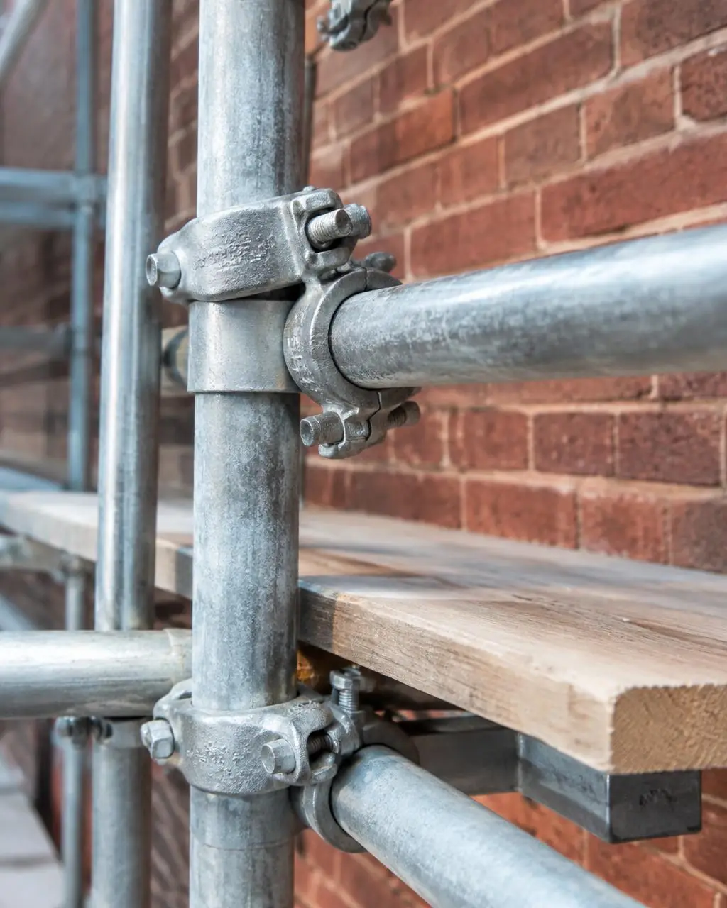 Close-up of scaffold tubes, couplers and boards against brickwork