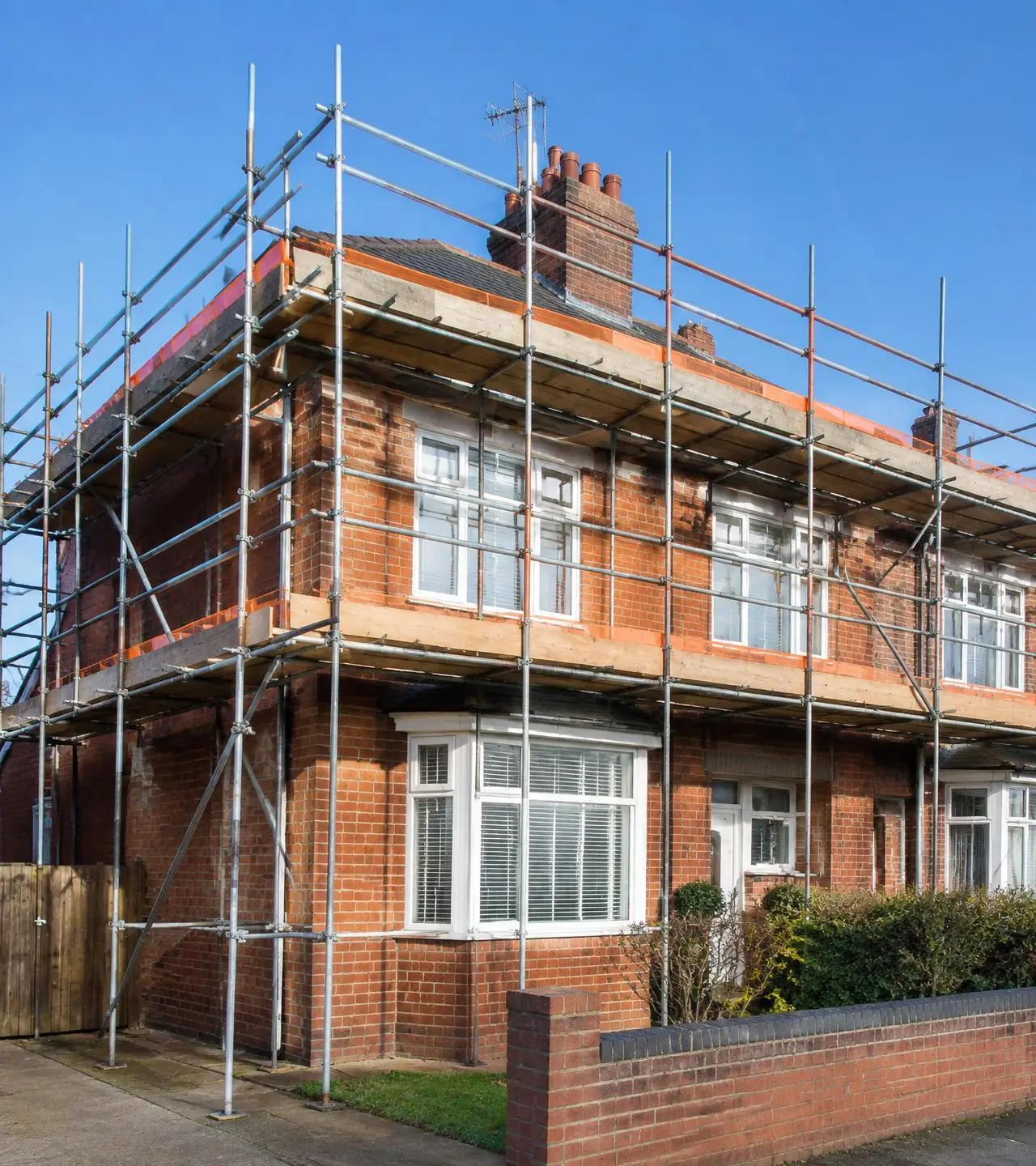 Galvanised scaffolding erected around a red-brick British semi-detached house